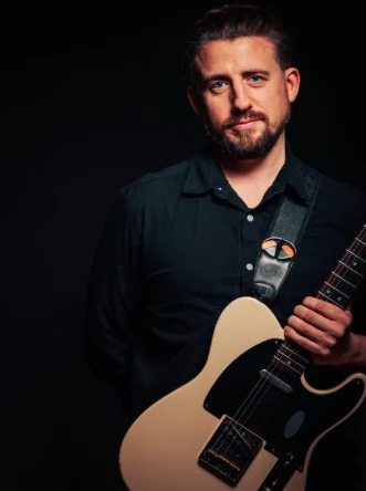 Portrait of Ryan Inglis holding an electric guitar