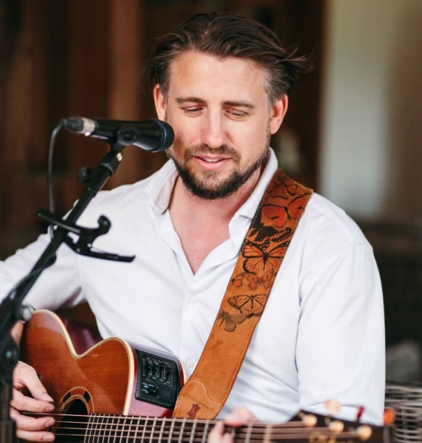 Ryan Inglis smiling while playing acoustic guitar