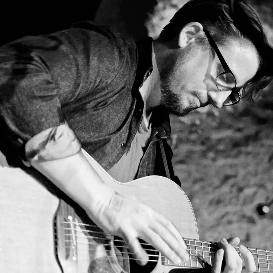 Black-and-white close-up of Ryan Inglis playing acoustic guitar